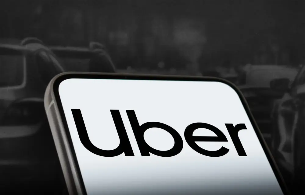 Close up of a smartphone screen displaying the Uber logo against a dark background, representing rideshare services and ongoing safety concerns.