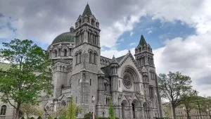 Cathedral Basilica of Saint Louis, a large historic Catholic cathedral with twin towers and a green dome, photographed from the front on a partly cloudy day.