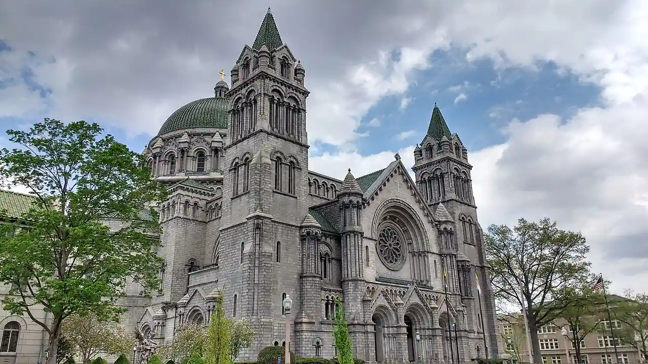 Cathedral Basilica of Saint Louis, a large historic Catholic cathedral with twin towers and a green dome, photographed from the front on a partly cloudy day.