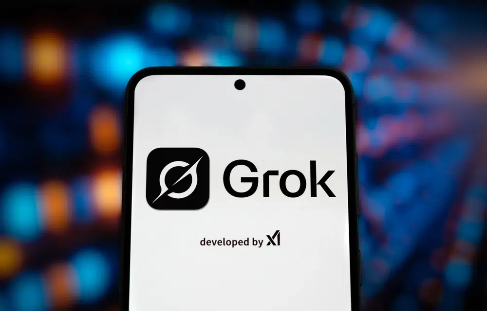 Smartphone displaying the Grok AI logo and branding on screen, developed by xAI, against a blurred digital background.