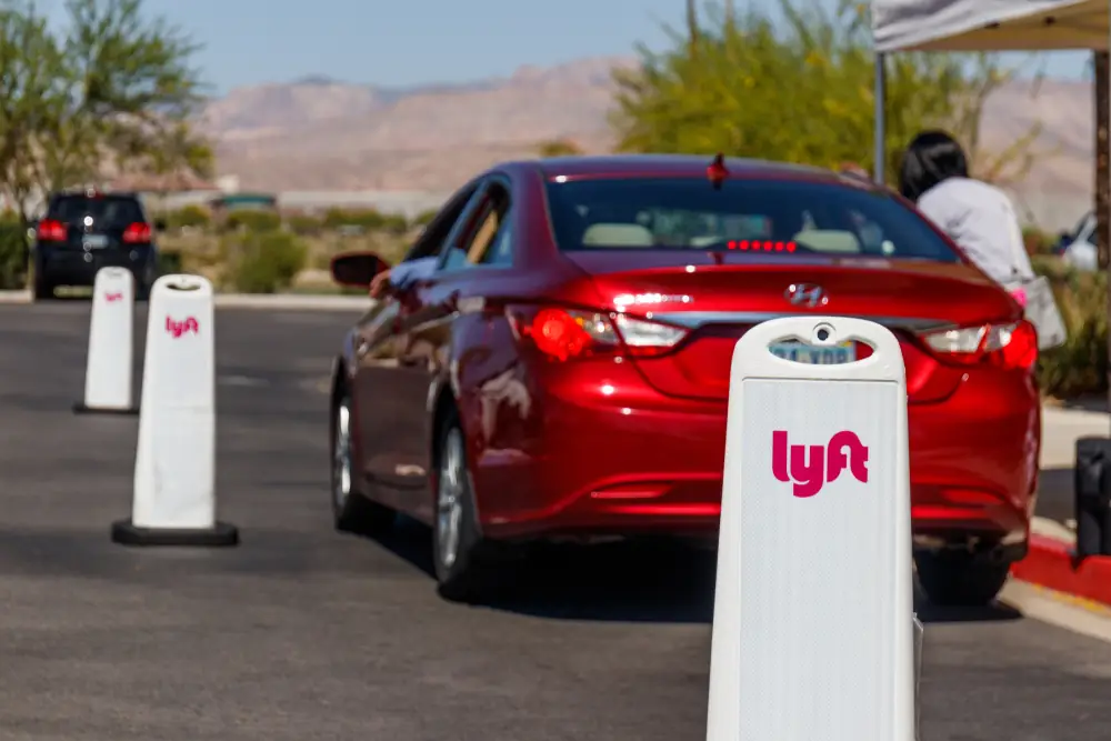 Lyft branded safety bollards lining a rideshare pickup area as a red car stops for passengers, illustrating Lyft operations and passenger safety at a pickup location.