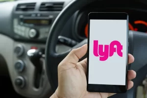 Hand holding a smartphone displaying the Lyft app logo inside a vehicle, representing rideshare use and passenger safety concerns.