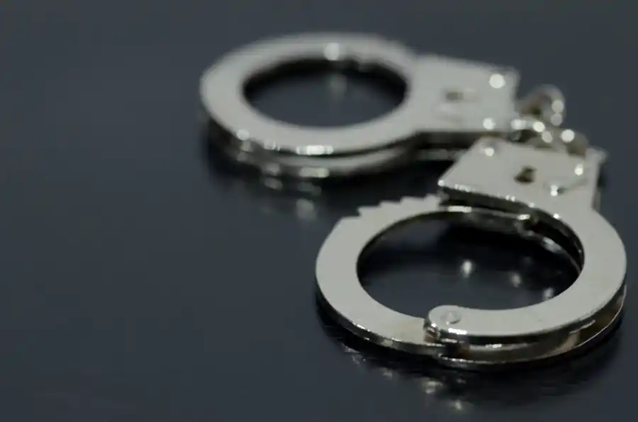 Handcuffs on a dark surface symbolizing arrests of school employees and a police officer in the Alabama child sexual abuse material investigation.