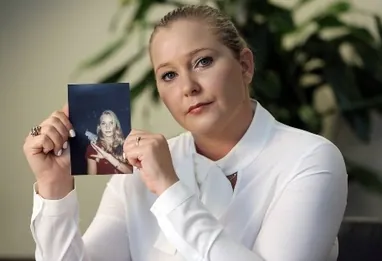 Virginia Giuffre holding a photograph of her younger self while speaking publicly about sexual abuse allegations.