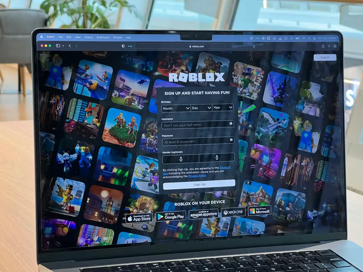 Laptop displaying Roblox sign-up screen with game thumbnails in the background