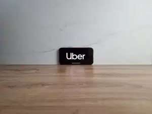 Your image has been converted to WebP format under 100KB: 👉 [Download the WebP image](sandbox:/mnt/data/uber-phone.webp) **Alt image text:** Smartphone displaying Uber logo on screen resting on a wooden surface against a neutral background