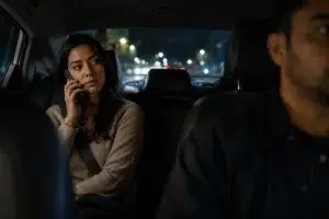 rideshare-passenger-phone-night-900w-q85 Female rideshare passenger in the backseat at night holding a phone to her ear while looking warily toward the driver.