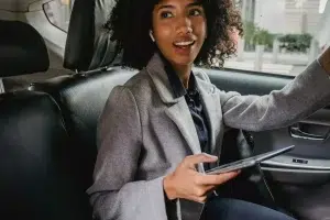 rideshare-passenger-california-uber-safety Woman riding in the back seat of a car while holding a phone, representing rideshare passenger safety concerns.