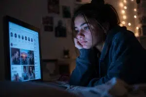 teen-social-media-screen Teen girl staring blankly at a social media feed on a laptop late at night.