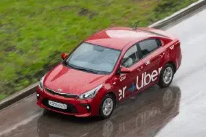 uber-taxi-tomsk Red Uber-branded Kia Rio driving on a wet road